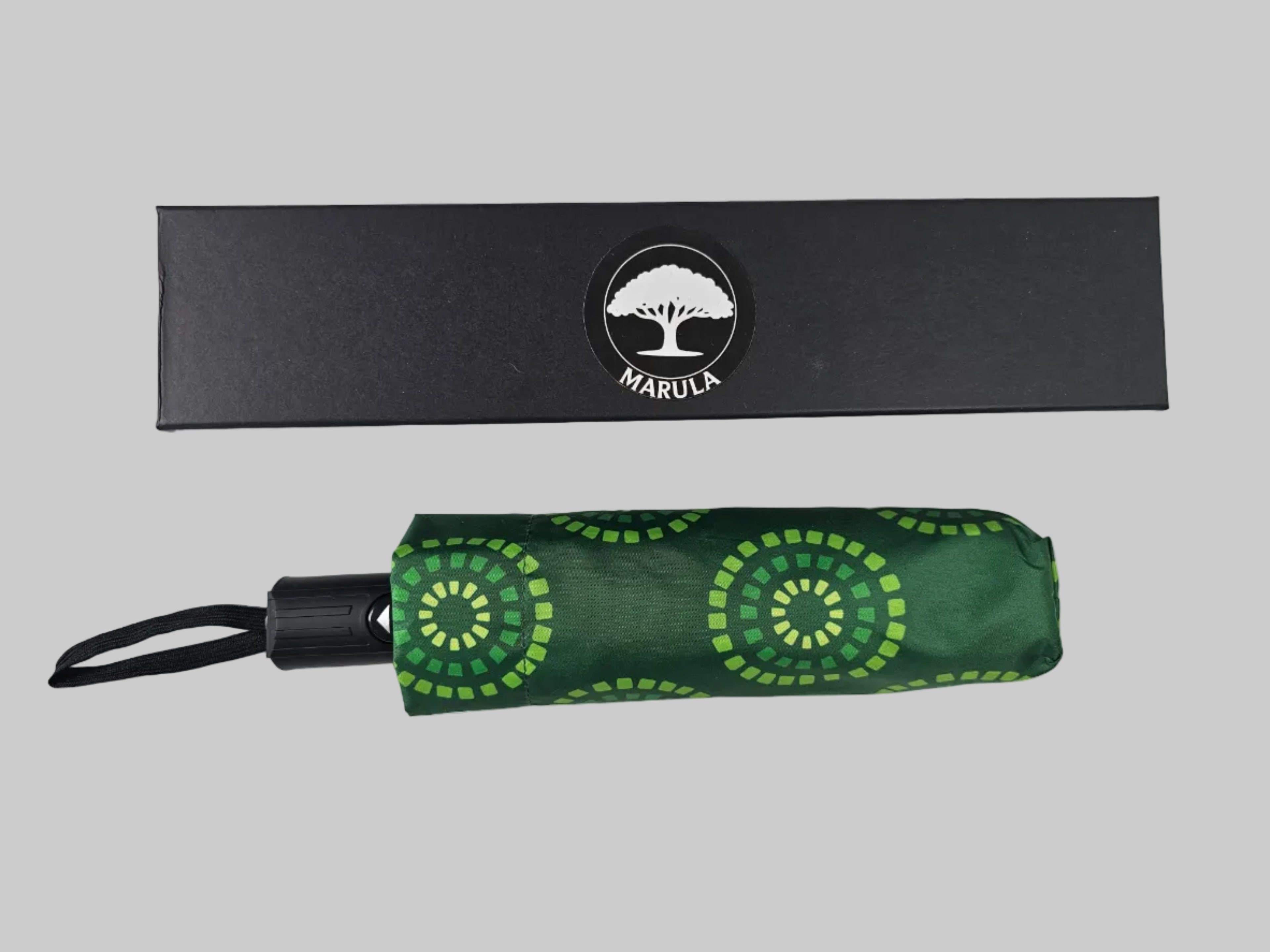 Green umbrella with circular patterns and black handle, placed in front of a black box with 'Marula' branding on a white background.